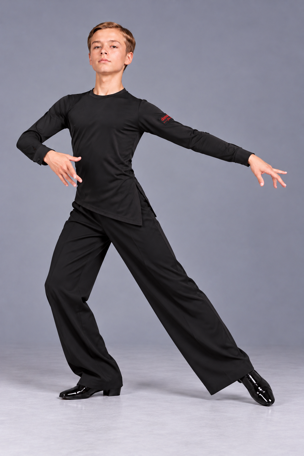 Boy performing a Latin dance step in a Diamond Fashion black dance set with an asymmetric long-sleeve top and flowing wide-leg trousers
