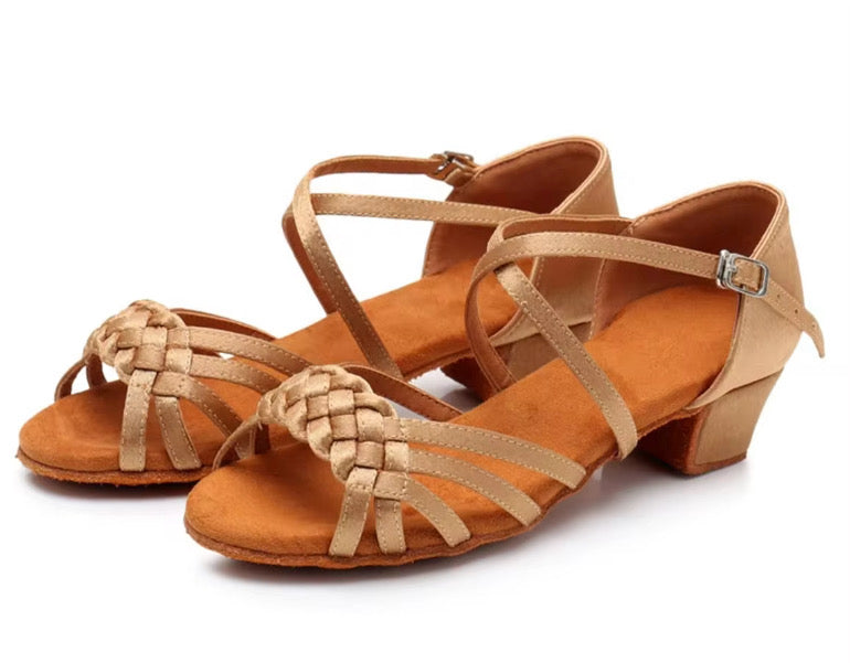 Light tan ballroom and Latin dance shoes for girls with braided straps and low heel on a light background